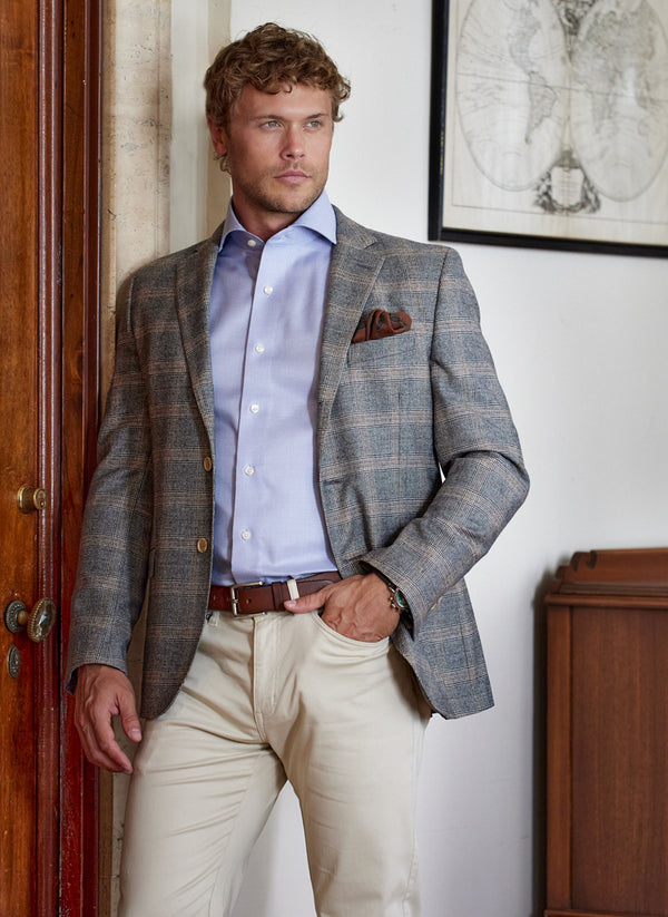 model wearing a solid blue shirt with a sports coat and featuring a paisly wool pocket square in rust
