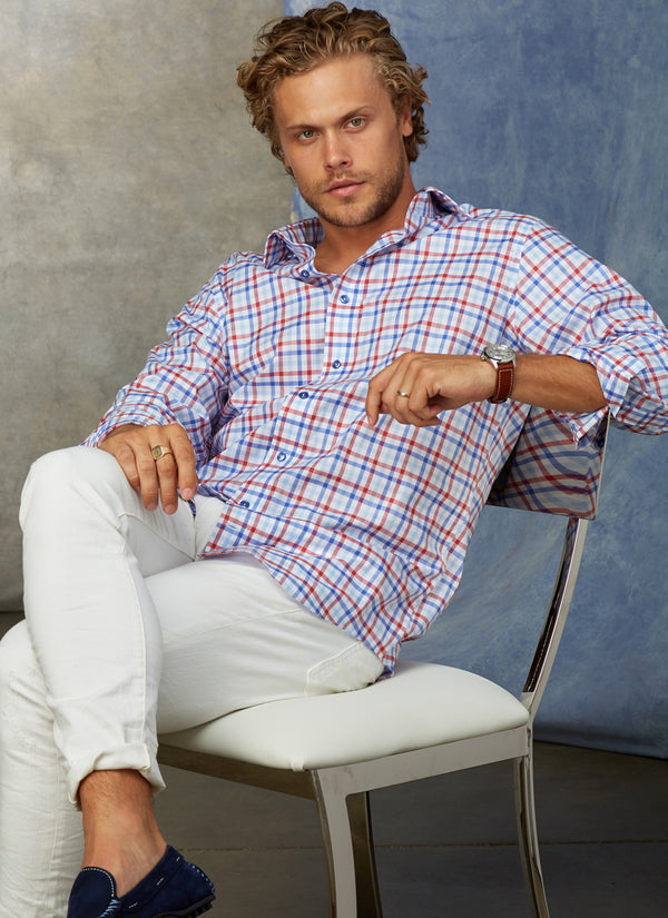 model wearing blue and red plaid shirt while in white pants and navy blue loafers while sitting