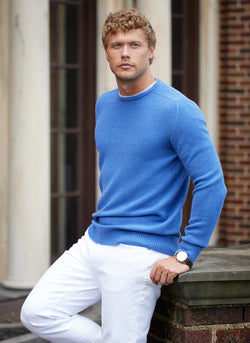 model leaning against brick wall in 100% merino wool crew neck sweater in jeans mélange and cream pants