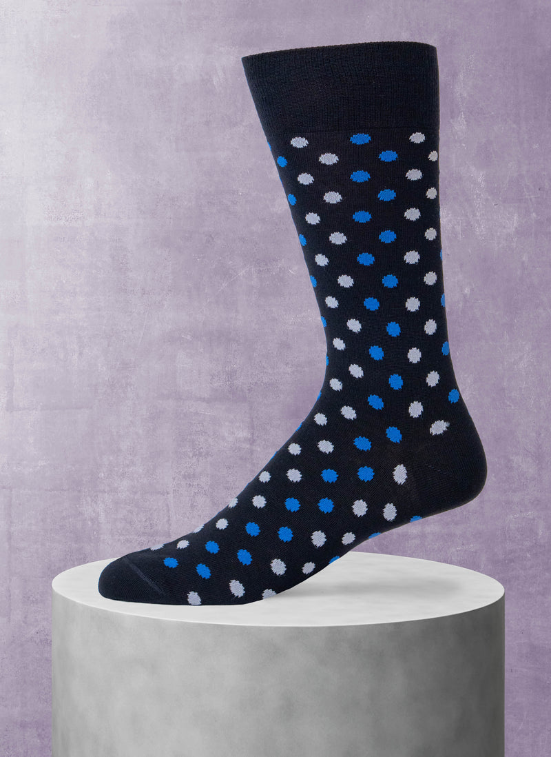 Black sock with blue and white polka dots on a gray pedestal against a purple background