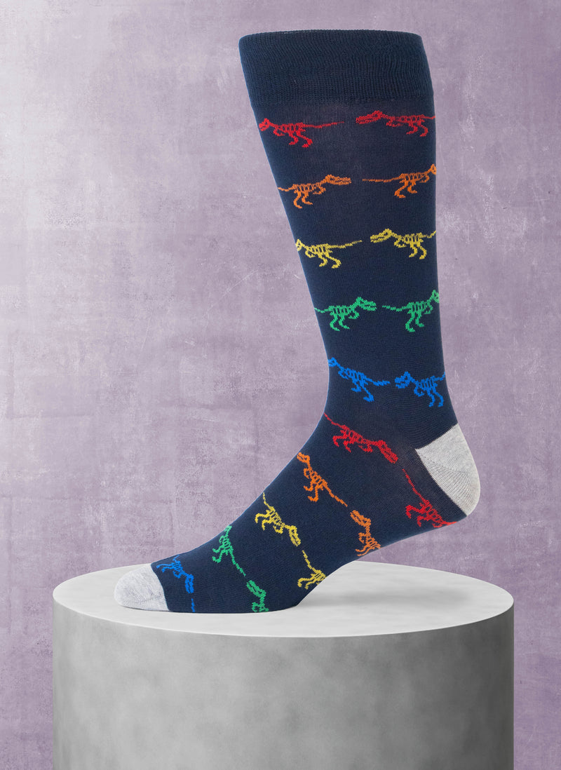 Navy sock with colorful dinosaur pattern on a gray pedestal against a purple background