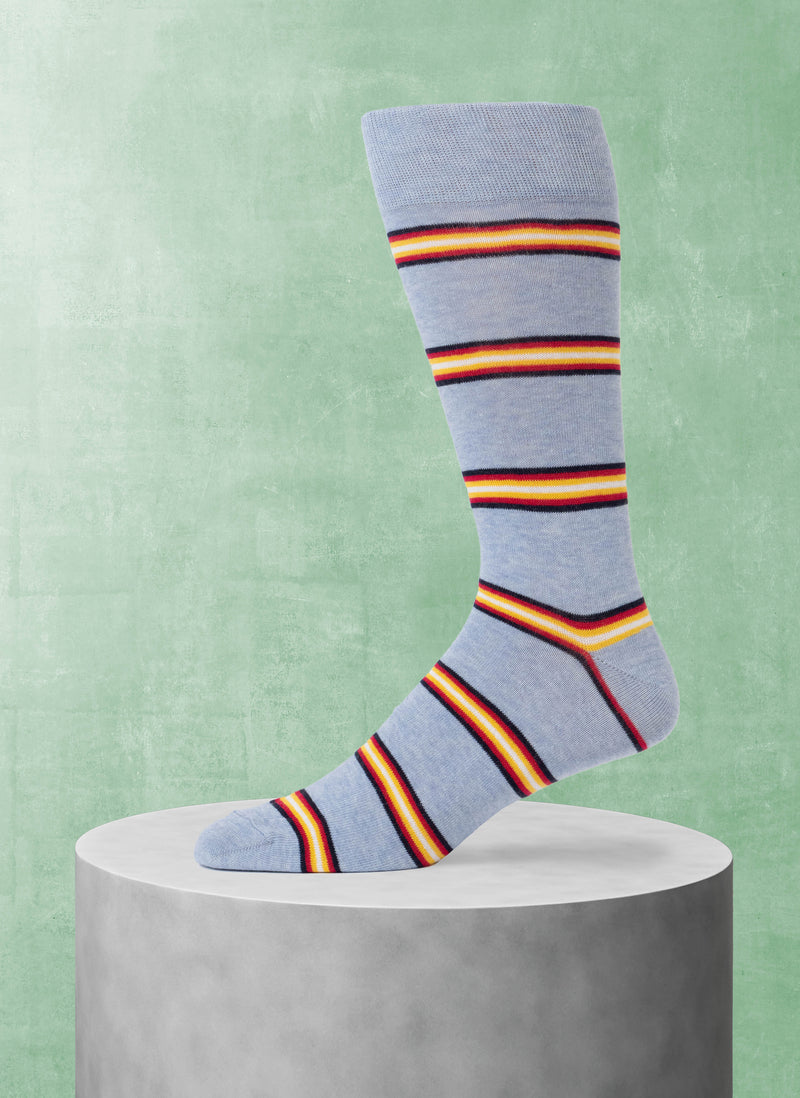 Light blue sock with multicolor stripes on a gray pedestal against a green background