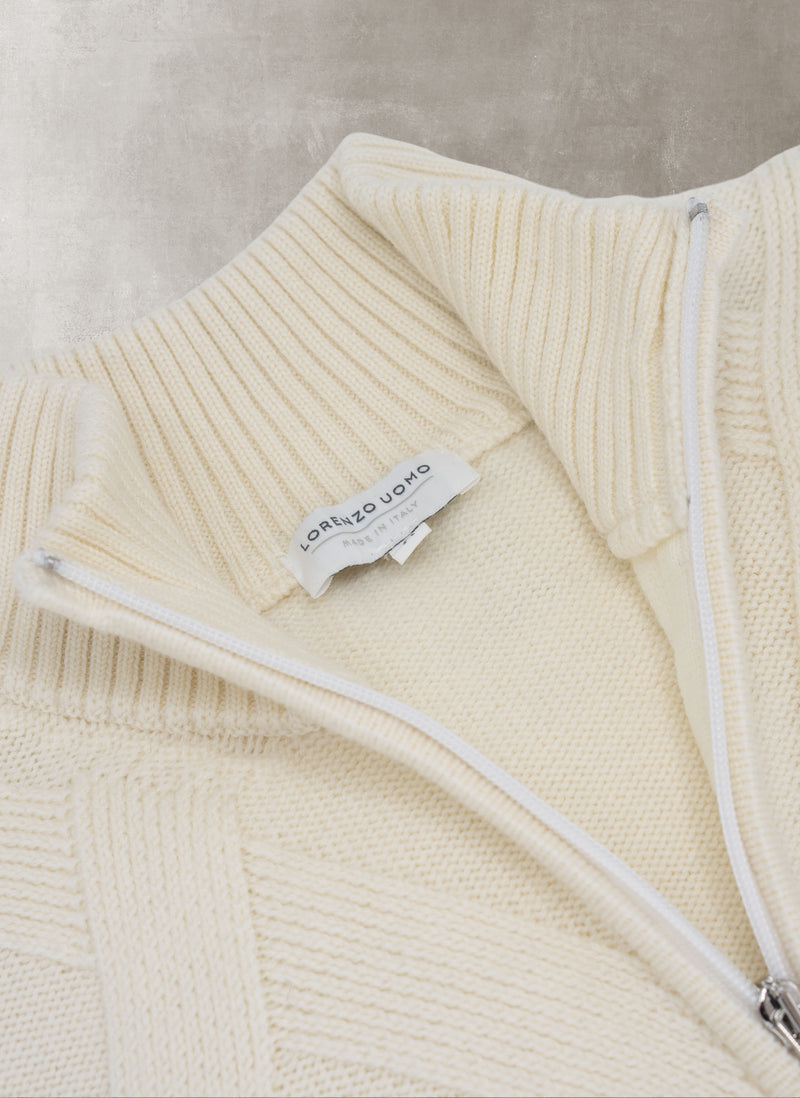 Close-up of a cream-colored sweater with a brand label on a neutral background