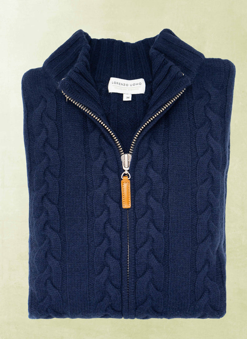 Folded navy blue cable knit sweater with a zipper on a light beige background