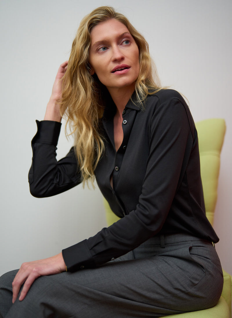 Woman wearing a black shirt and gray pants sitting on a yellow chair against a plain background