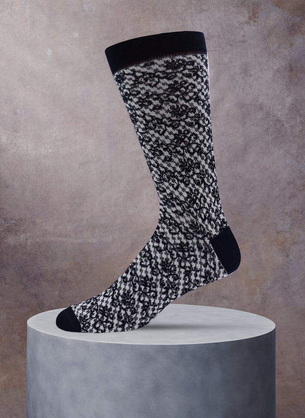 Black and white patterned sock on a gray pedestal against a beige background