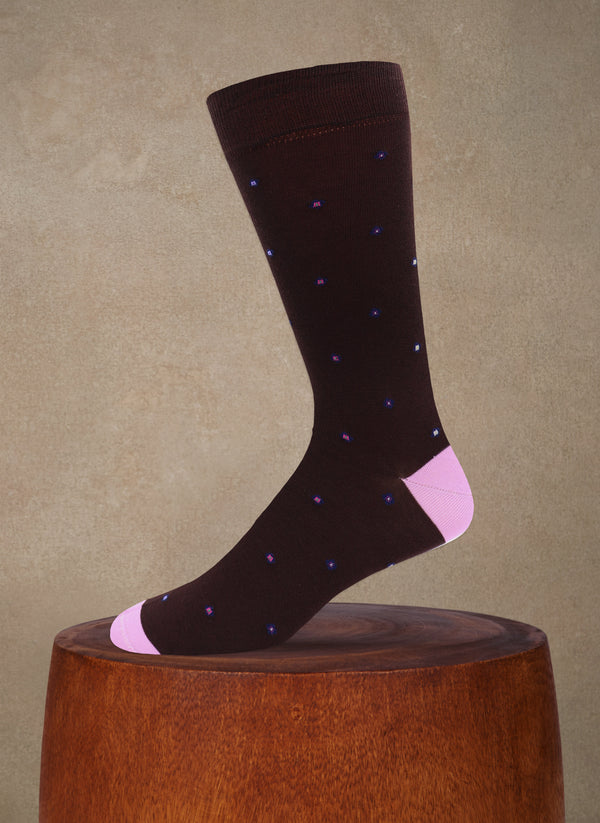 Dark brown sock with pink accents on a wooden block against a beige background
