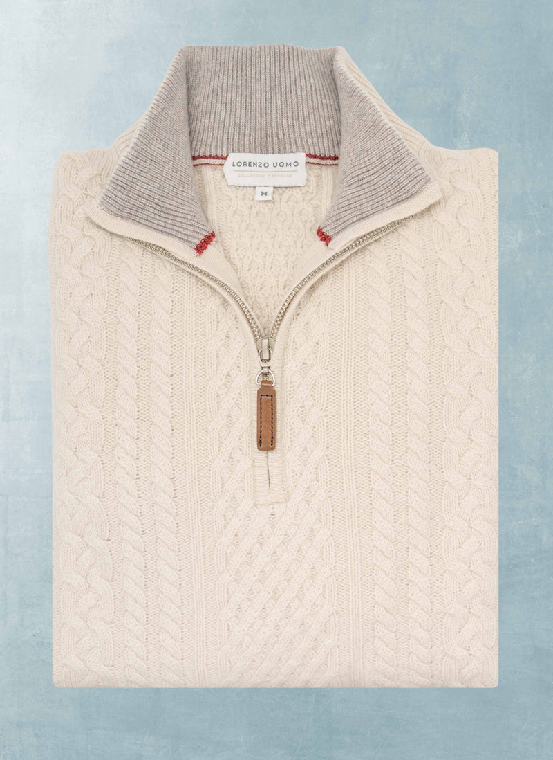 Beige cable knit sweater with a quarter zip on a light blue background