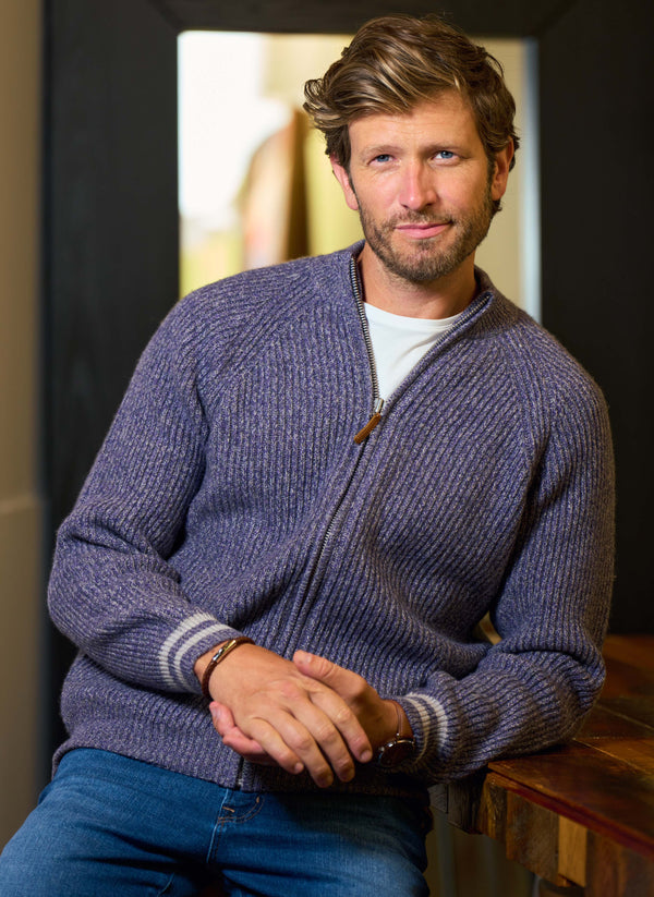Man wearing a purple sweater sitting indoors with a neutral background