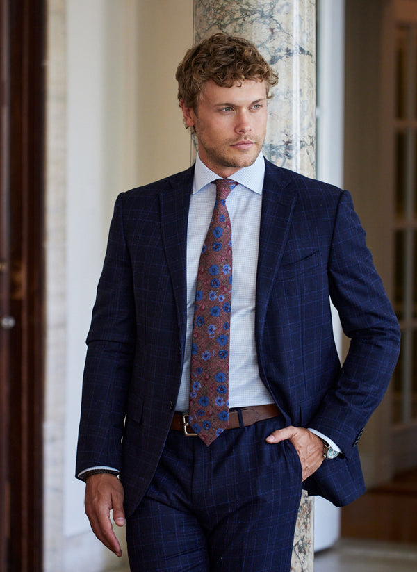 model wearing a navy blue windowpane suit with a printed wine flower tie