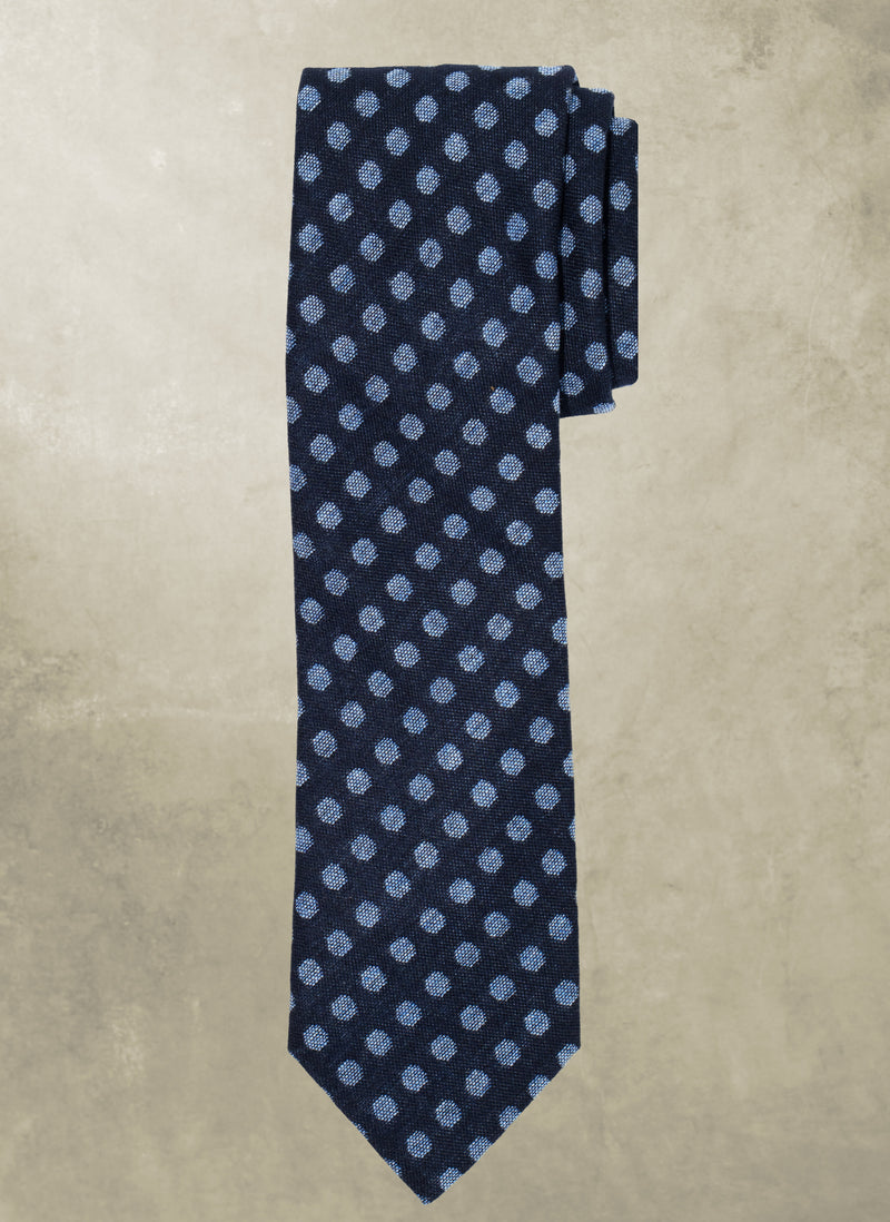 Navy blue tie with light blue polka dots on a beige background