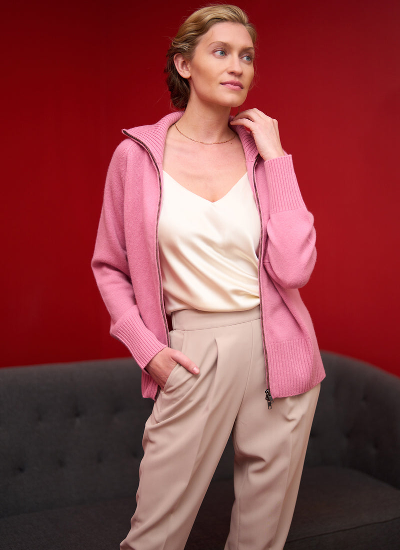 Woman wearing a pink cardigan over a white top and beige pants against a red background
