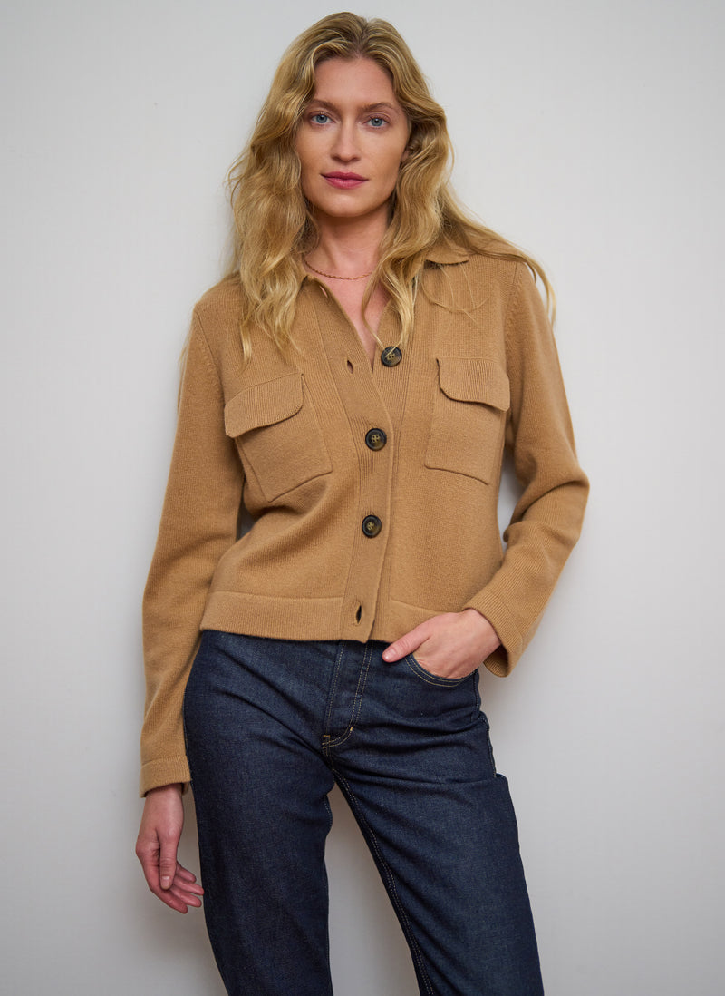 Woman wearing a tan jacket and blue jeans against a plain background