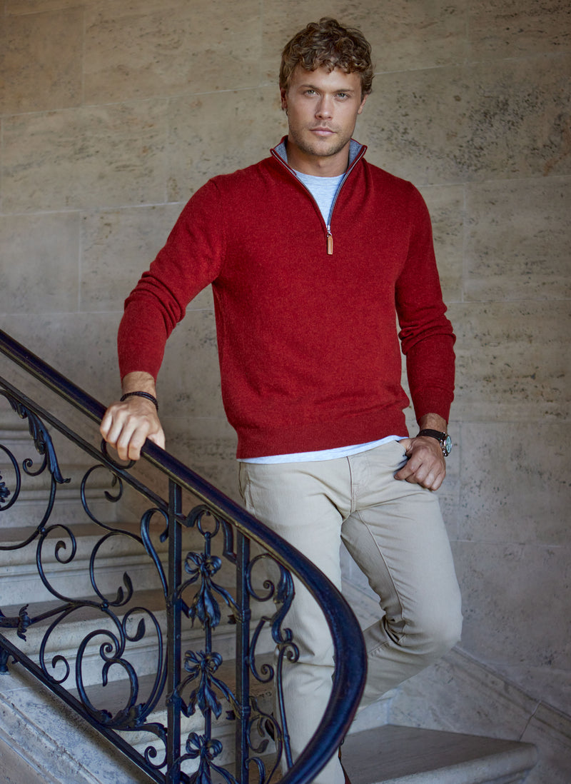 model standing on stair case featuring a light grey crew neck undershirt, quarter zip cashmere sweater in cinna, and khaki pants