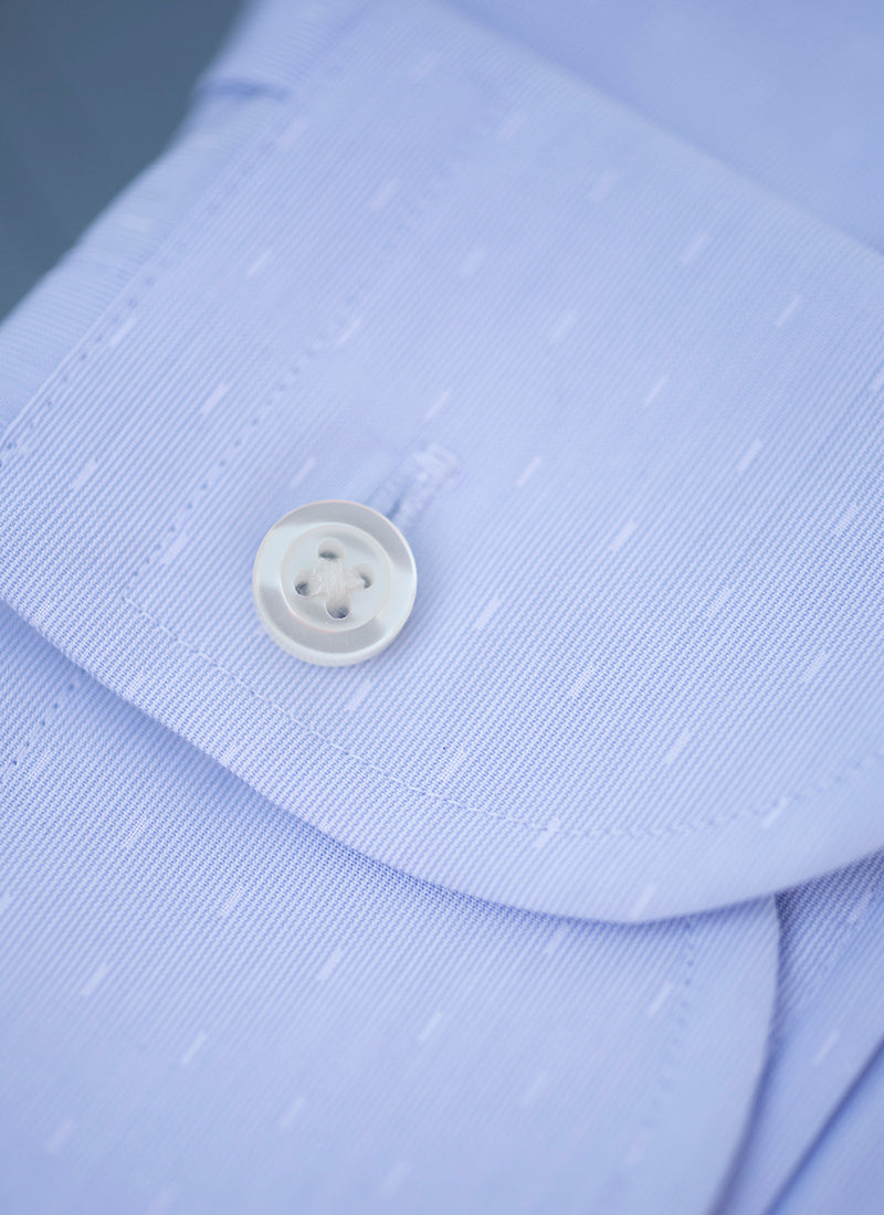 cuff close up detail of blue dash shirt with white button and button threads. 