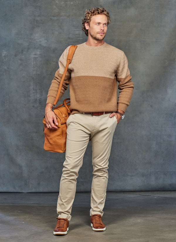 modeling our men's dolomite cashmere herringbone sweater in tonal camel with a leather travel bag on shoulder 
