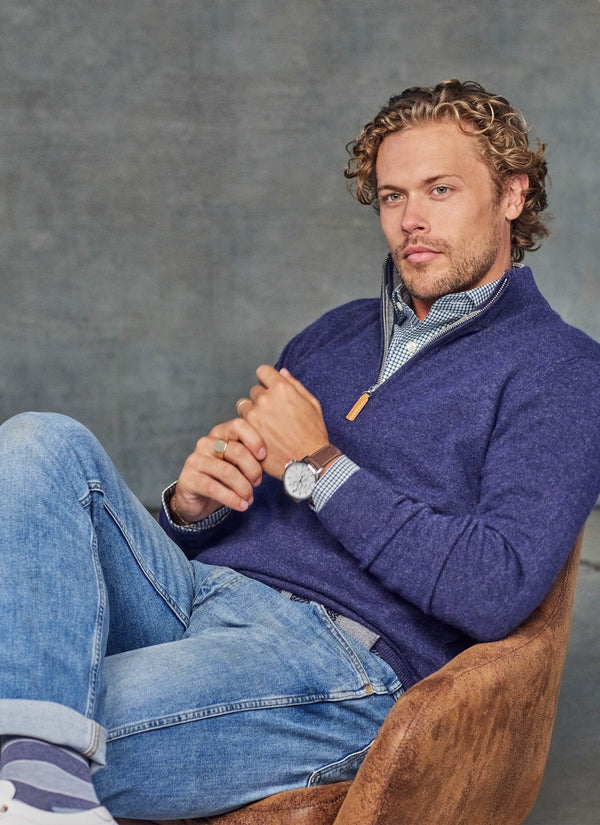 model wearing a quarter zip cashmere sweater in navy while sitting on a brown chair