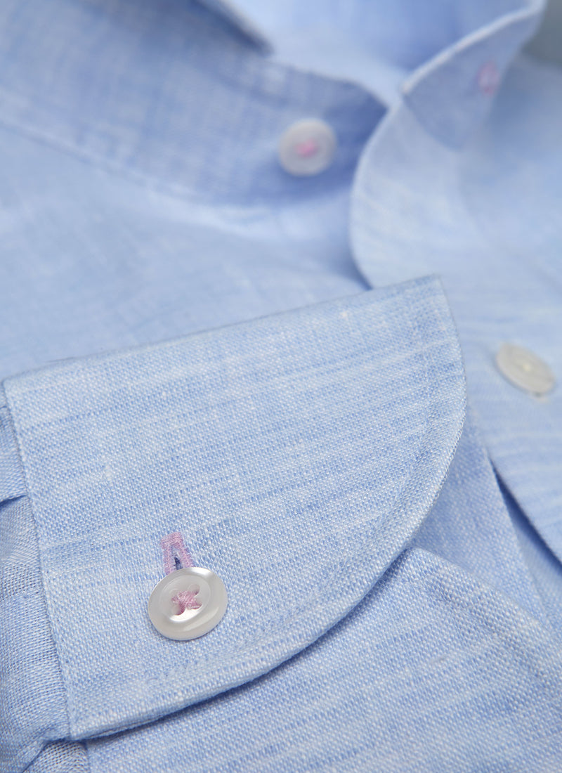 detailed close up of blue linen shirt cuff with  pink button holes and button thread and white buttons